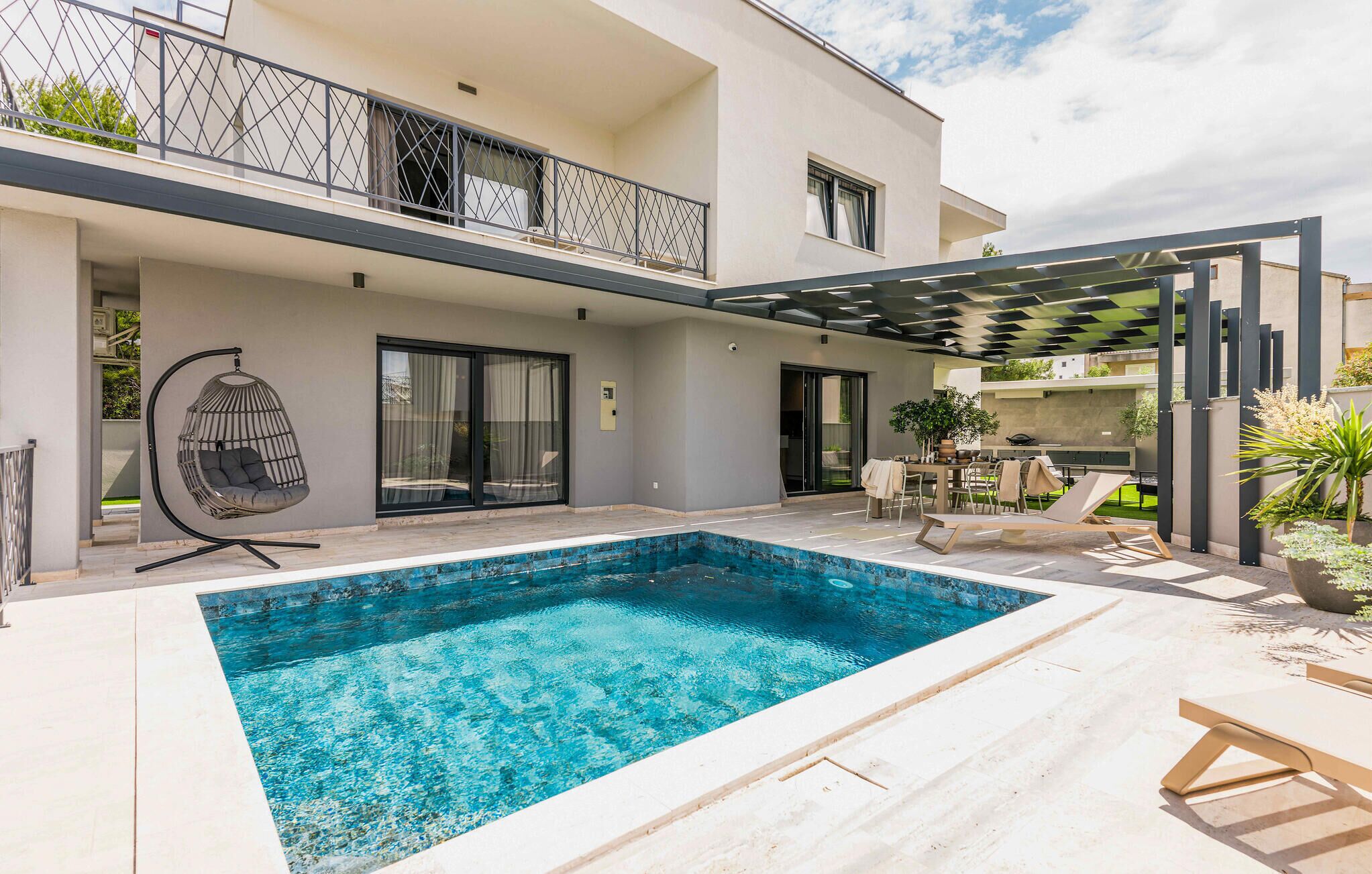 Una moderna casa a due piani con piscina, area salotto esterna e una pergola.