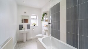 A modern bathroom with a white sink, toilet, and bathtub, and grey tiled walls.
