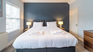 A neatly made bed with white linens, two bedside lamps, and a dark blue headboard.