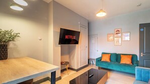 A modern living room with a flat-screen TV, a sofa, a coffee table, and a dining area.