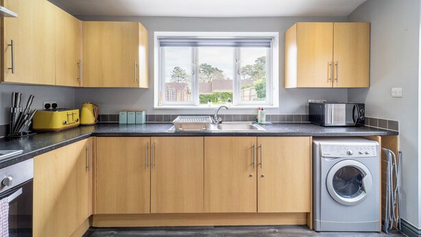 A modern kitchen with wooden cabinets, a built-in washing machine, and a window providing natural light.