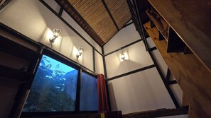 A room with a large window, wooden beams, and wall-mounted lights. - Casa del Árbol Hostel Xochimilco (Oaxaca)