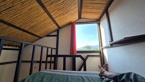 Una habitación con techo inclinado, una ventana con cortina roja y una cama con manta verde.