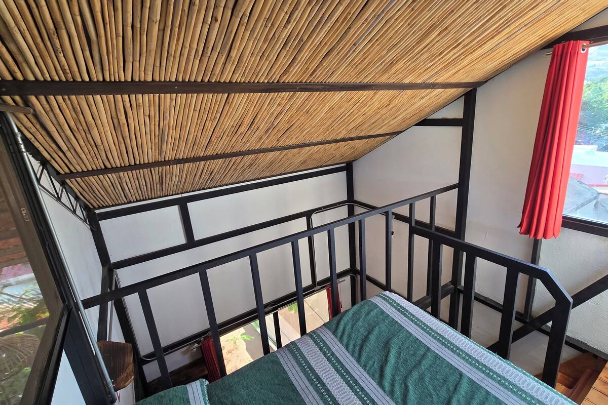 A room with a bamboo ceiling, a metal railing, and a view of a hillside.