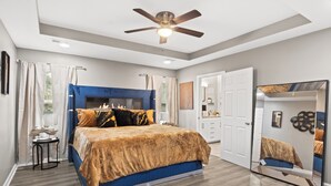 Une chambre à coucher avec un lit, un ventilateur de plafond, un miroir et une porte.