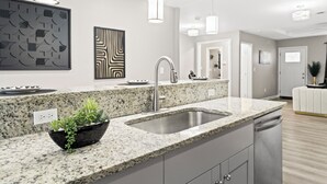 Une cuisine moderne dotée de plans de travail en granit, d’un évier en acier inoxydable et de luminaires suspendus.