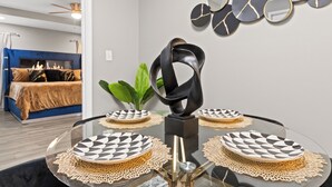 Un espace repas moderne avec une table en verre, des assiettes aux motifs géométriques en noir et blanc, et une sculpture abstraite noire.