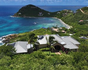 A coastal property with multiple buildings, a beach, and a small island in the background. - Introducing Blue View (Cruz Bay)