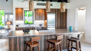 A modern kitchen with a large island, wooden bar stools, and pendant lighting. - Introducing Blue View (Cruz Bay)