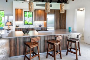 A modern kitchen with a large island, wooden bar stools, and pendant lighting. - Introducing Blue View (Cruz Bay)