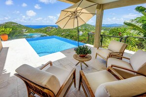 A pool area with a view of the ocean and hills, surrounded by lounge chairs and a potted plant. - Introducing Blue View (Cruz Bay)