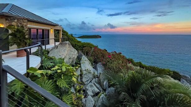 A coastal property with a stone facade, a balcony with a railing, and a view of the sea and a small island. - Introducing Blue View (Cruz Bay)