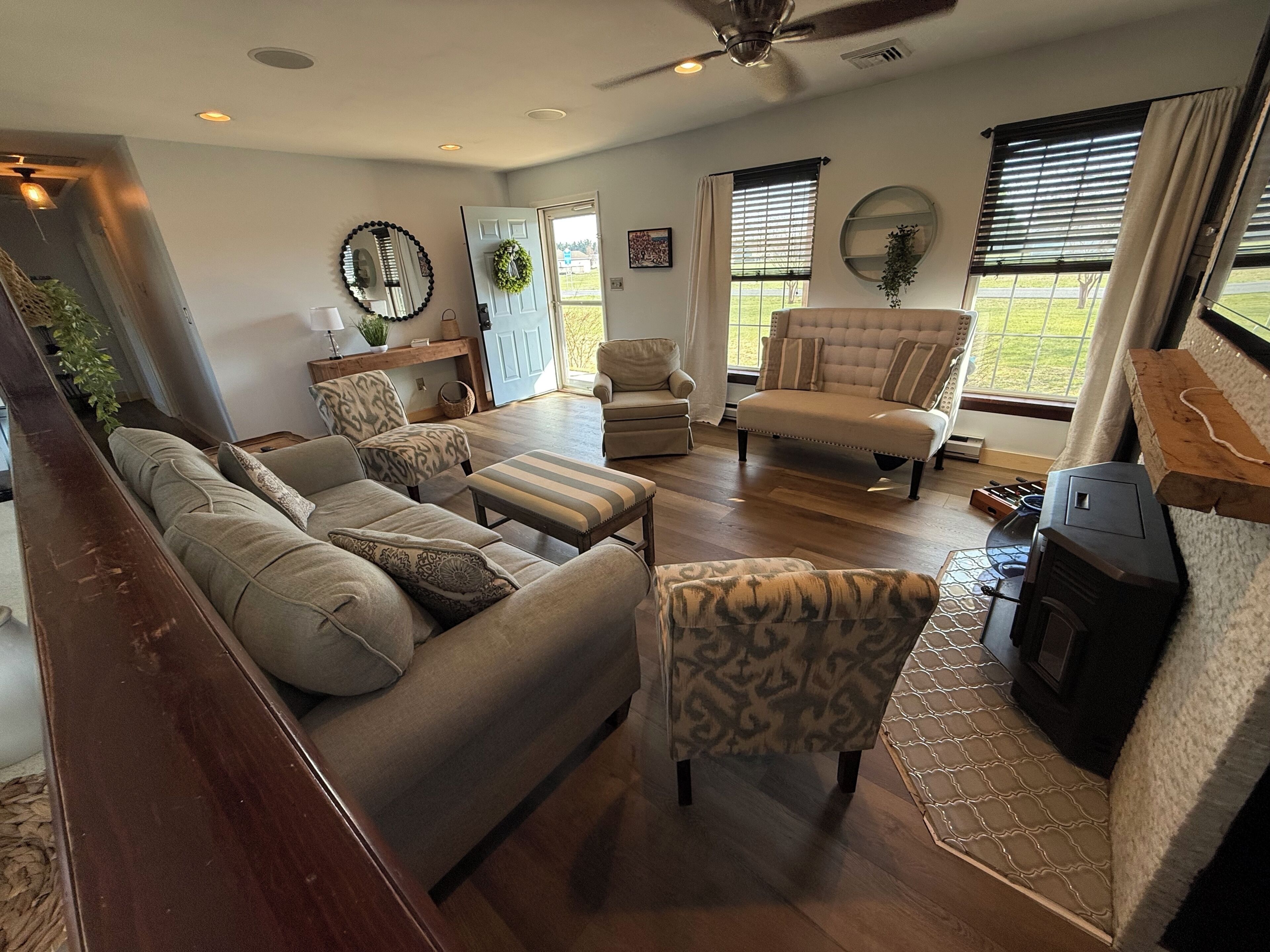 A spacious living room with a sofa set, patterned chairs, a fireplace, and a ceiling fan.