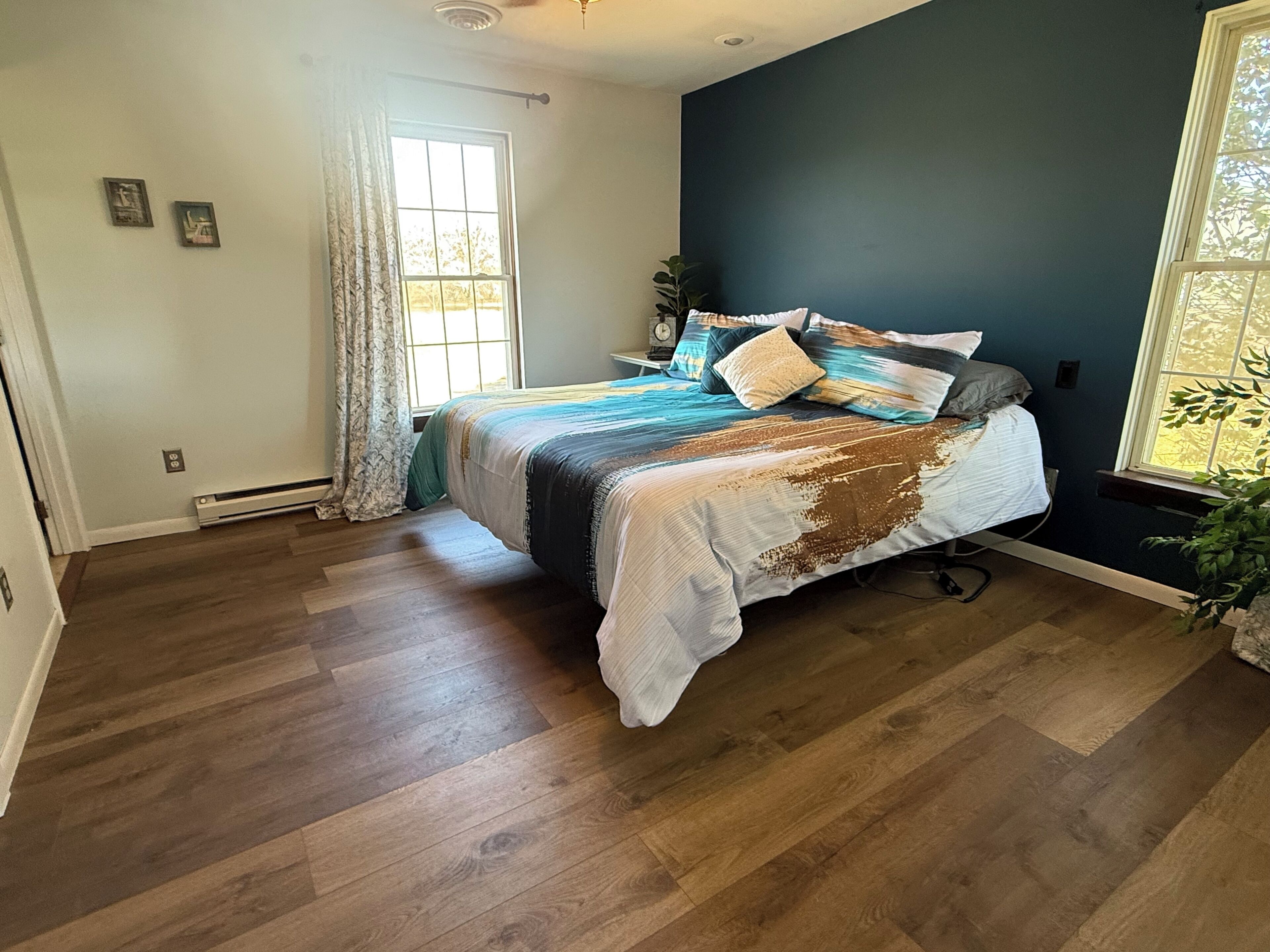 Ein Schlafzimmer mit Bett, Holzboden, Fenster und einer Pflanze.