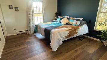 Ein Schlafzimmer mit Bett, Holzboden, Fenster und einer Pflanze.