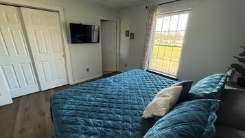A bedroom with a bed, a ceiling fan, a TV, and a window with a view.