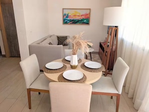 A dining area with a round table, four chairs, and a vase with dried plants.