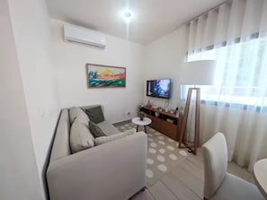 A modern living room with a sofa, a small round table, a TV, and a painting on the wall.