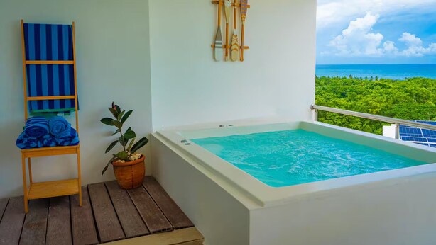 Een balkon met een jacuzzi, een houten stoel met een blauwe handdoek en een potplant.