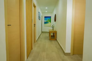 A hallway with wooden doors, a small table with a plant, and a painting on the wall.