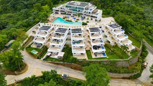 Een modern resort met meerdere witte gebouwen, een centraal gelegen zwembad en zonnepanelen op de daken.