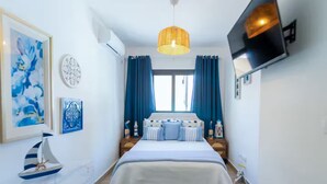 Une chambre à coucher avec un lit, un luminaire suspendu, un téléviseur fixé au mur et des œuvres d’art accrochées au mur.