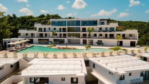 Un hôtel moderne à plusieurs étages, doté d’une piscine sur le toit, de nombreux balcons et d’une végétation luxuriante en arrière-plan.