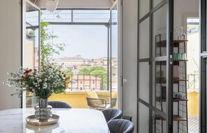 A balcony with a view of buildings, a table with a vase of flowers, and a chair. - IMMERSE YOURSELF IN THE AUTHENTIC RHYTHM & ATMOSPHERE OF ROME NEAR COLOSSEUM (Roma)