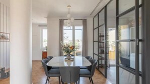 En moderne spisestue med et stort bord og stole, en vase med blomster og store vinduer med udsigt til det fri.