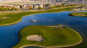 A golf course with bunkers and a water hazard, surrounded by a residential area with buildings.