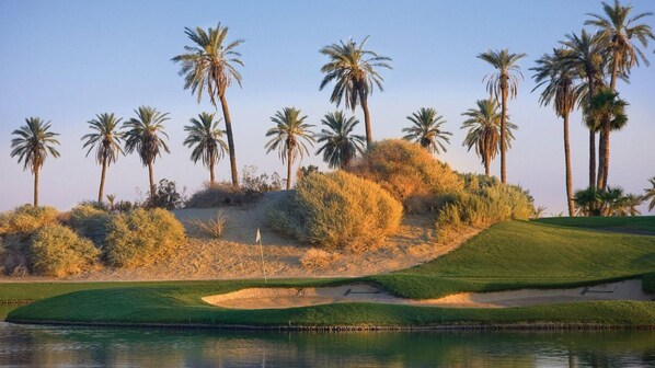 A golf course with sand bunkers, water hazards, and palm trees.
