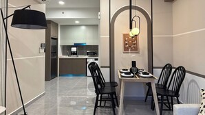 Una cocina moderna con microondas, cafetera y lavadora. Cuenta con un comedor con mesa y sillas, y una lámpara colgante sobre la mesa.