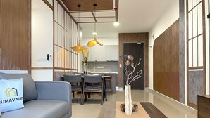 A modern living room with a sofa, dining table, and chairs. There is a decorative tree in a vase and a wooden floor. - Ancestry 3BR @ M Vertica | MRT Access+Netflix+WiFi (Cheras)