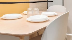 A modern dining area with a wooden table set for four, white chairs, and pendant lights with wooden shades. - Narrow Nest 2BR Continew Residence Wi-Fi + Netflix (Kuala Lumpur)