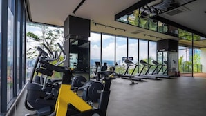 A gym with cardio machines, weightlifting equipment, and large windows offering a city view. - Narrow Nest 2BR Continew Residence Wi-Fi + Netflix (Kuala Lumpur)