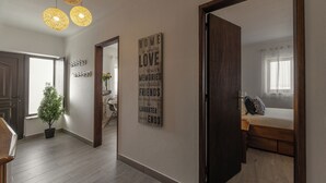 A hallway with a wooden floor, a potted plant, a bed with a window, and a wall with a motivational quote. - Lagoon View Villa - Ocean Serenity (Óbidos)