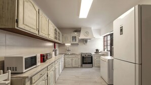 A kitchen with white cabinets, a microwave, a stove, and a refrigerator. - Lagoon View Villa - Ocean Serenity (Óbidos)