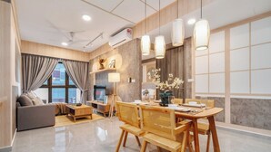 Una sala de estar moderna con un sofá, una mesa de comedor y sillas. Hay un televisor, una lámpara y un jarrón con flores.