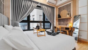 Et moderne hotelværelse med en stor seng, et træskrivebord og udsigt til byen gennem store vinduer.