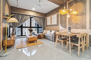 Un salon moderne comprenant un canapé, une table basse et une table à manger. On y trouve une grande fenêtre avec des rideaux, un ventilateur de plafond et un luminaire décoratif.