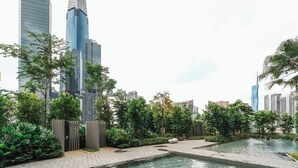 Eine moderne Stadtlandschaft mit hohen Gebäuden, einem Wasserspiel und üppiger Vegetation.