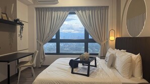 Ein Hotelzimmer mit Bett, Schreibtisch, Stuhl und Blick auf eine Stadtlandschaft durch große Fenster.