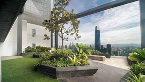 Um jardim no terraço com grama sintética, vasos com diversas plantas e vista para a cidade.