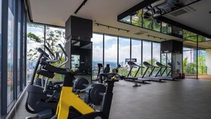 Academia com máquinas de cardio, equipamentos de musculação e amplas janelas com vista para a cidade.
