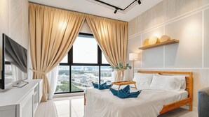Quarto de hotel moderno com uma grande janela, cama com roupa branca, mesa de cabeceira com um vaso e TV de tela plana sobre um móvel branco.