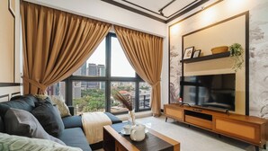 Ein modernes Wohnzimmer mit großem Fernseher, einer Couch, einem Couchtisch und Blick auf die Stadt durch große Fenster.