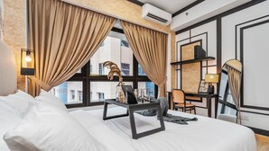 Habitación de hotel con una cama grande, un escritorio con una silla, una lámpara y vistas a la ciudad a través de amplios ventanales.