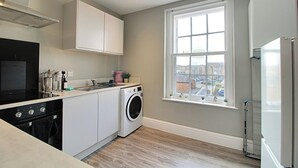 A compact kitchen with a washing machine, a stove, and a window with a view. - Regent Parade Retreat, sleeps 6, Free parking, (North Yorkshire)