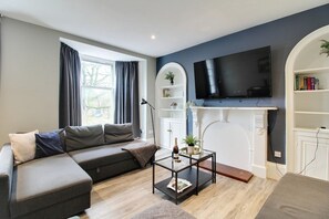 Una sala de estar moderna con un sofá seccional, una mesa de centro de vidrio, una chimenea, un televisor montado y una estantería.