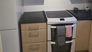 A compact kitchen with light wood cabinets, a white refrigerator, a stove with a hood, and a small oven. - Modern 2-Bed Apt Near Hospital and University of Birmingham (Birmingham)